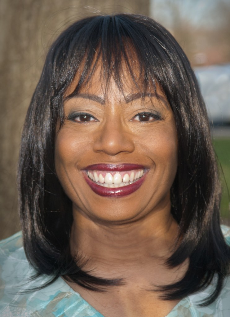 Headshot of a smiling woman with straight black hair and light makeup, wearing a teal top.
